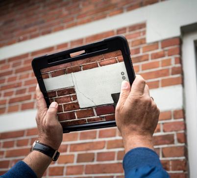 Met een tablet wordt een foto gemaakt van een scheur in een buitenmuur. 