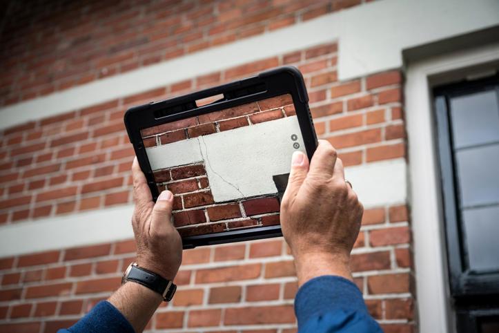 Met een tablet wordt een foto gemaakt van een scheur in een buitenmuur. 