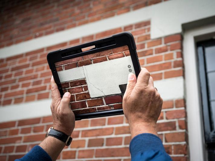 Met een tablet wordt een foto gemaakt van een scheur in een buitenmuur. 