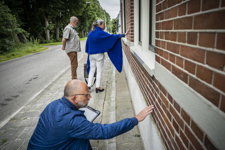 Op straat bekijken drie personen een woning en twee ervan houden hun hand tegen de buitenmuur.