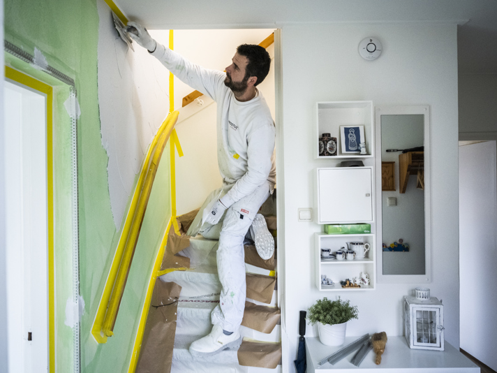 Persoon stukt een wand naast de trap naar de bovenverdieping in een huis.