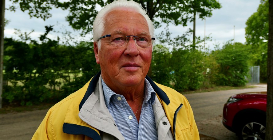 Hans Oskam staat buiten, op de achtergrond een groene heg en bomen