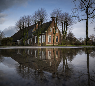 De boerderij in Tinallinge van voren gezien, weerspiegeld in een grote plas water.