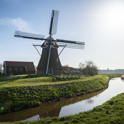 Molen langs een groen Gronings dijkje met een sloot ernaast