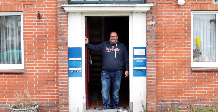 Marcel Swart bij de voordeur van zijn huis, de mat is een Groningse vlag, ernaast staan klompen