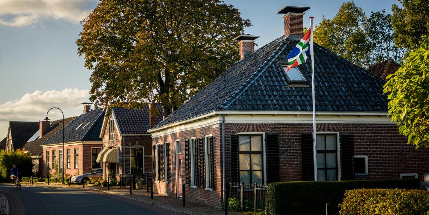 Aantal oude huizen in straat met de vlag van Groningen in een tuin