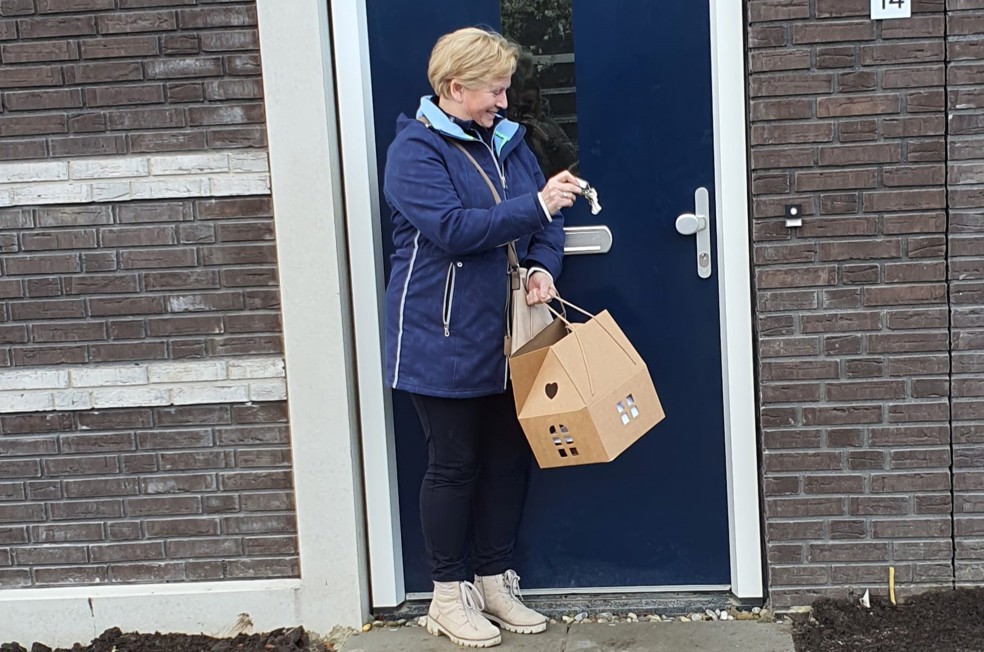 Jeanne Schoonhoven staat lachend met de sleutel in haar hand bij de voordeur van haar nieuwe woning