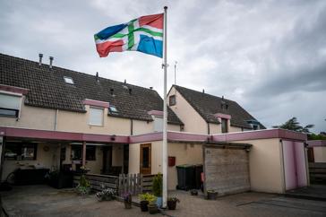 De Groningse vlag wappert bij een rij roze huizen in Sappemeer