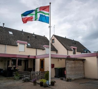 De Groningse vlag wappert bij een rij roze huizen in Sappemeer