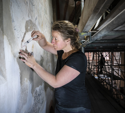 Restaurator Aafje Bouwhuis spuit heel precies mortel in een scheur in de muur van de Mariakerk.